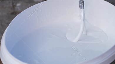 Mixer for construction liquids is placed into bucket with white paint