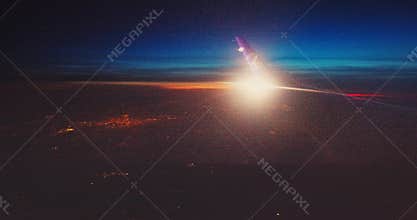 Flying with airplane over sunset horizon with clouds and land of city lights below