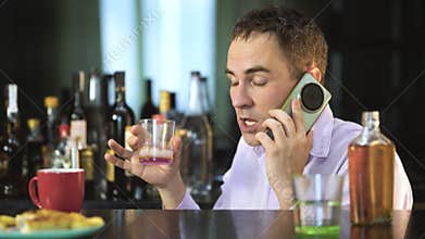 An evil drunk businessman talking on phone while holding a glass of alcohol in his hands at a bar in the evening