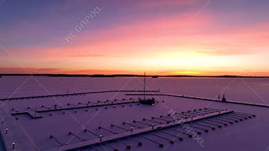 Aerial View of dead frozen harbour docks with boat and ice below at sunrise or sunset. Extreme cold weather.