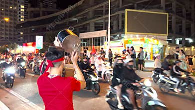 Nha Trang, Vietnam - January 5, 2025: A Vietnamese fan bangs on a saucepan amidst the bustling street, surrounded by