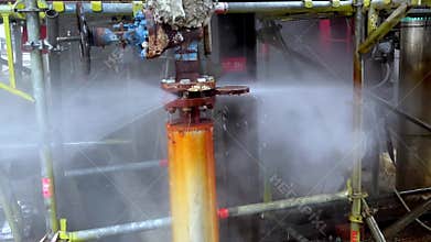 Close-up view of a leaking valve inside a factory infrastructure releasing steam and spraying water