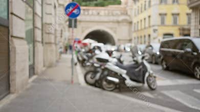Blurry street scene in rome, italy features parked scooters, cars, and historic architecture with a bustling urban atmosphere