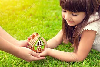 little girl and a woman hands holding small house on a background of green grass