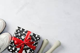 Fitness gift with red ribbon, white sneakers, and dumbbells on marble background.