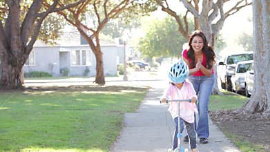 Mother Teaching Daughter To Ride Scooter
