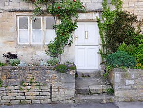 Exterior view of an old stone cottage house on a street in an English village.