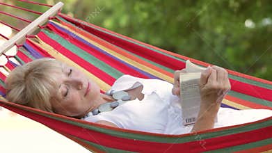 Senior Woman Relaxing In Hammock With Book