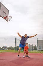 A father stands in a defensive position playing basketball with his little daughter.