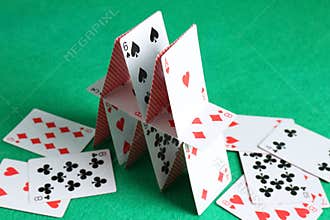Collapsed house of playing cards on green background, closeup