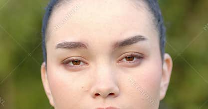 Asian woman in twenties raising gaze, blinking, furrowing brow, holding eye contact at garden