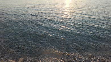 Calm sea waves gently lapping on the pebble beach of Calabria, Italy, during a golden sunset