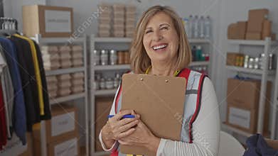 Woman holds clipboard and smiles at donation center shelves filled with clothes and cans; compassion service