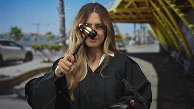 Woman judge wearing robe bangs a wooden gavel on a sound block at outdoor airport terminal gate area; justice authority fairness