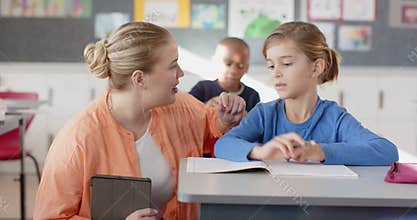 In school, female teacher helping student with writing assignment in classroom