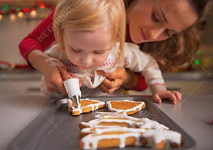 Baby helping mother decorate christmas cookies with glaze