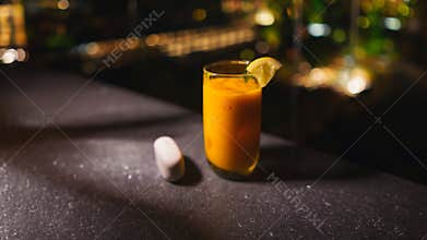 Refreshing orange cocktail with a lemon garnish on a dark bar counter, with blurred background lights