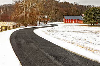 long winding curved road or driveway leading to red barns covered in snow