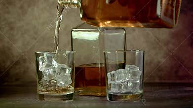 Glasses of whiskey with ice and a bottle of whiskey or brandy on a wooden table.