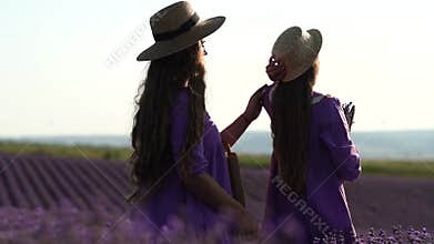 Mother and daughter in purple dresses are standing in a field of lavender. One of them is fixing the other's hair