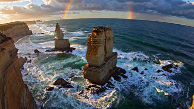 Scenic view of twelve apostles rock formations with rainbow on great ocean road, dramatic sunset. Natural landmark and