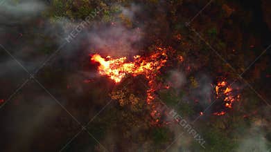 Aerial footage shows a wildfire rapidly spreading through dry forests and fields. Thick black smoke covers the landscape