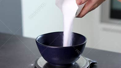 Close up of a female pouring white sugar into a blue bowl in the kitchen