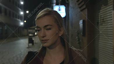 Beautiful blond woman in coat walking alone outdoors at night. Grain. Slow motion.
