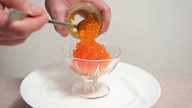 A hand scooping red caviar on a white background with a spoon.