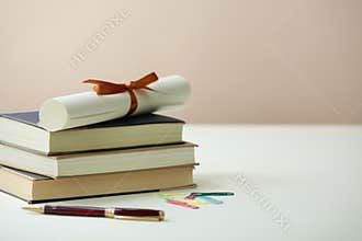 Books Stacked Together With Ribbon and Rolled Paper Beside Pen and Colorful Clips on Table