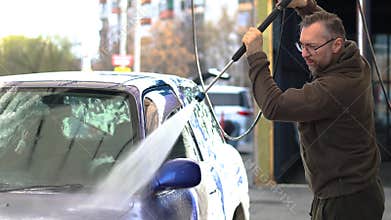 4K footage of a middle aged man washes a blue car at a self-service car wash