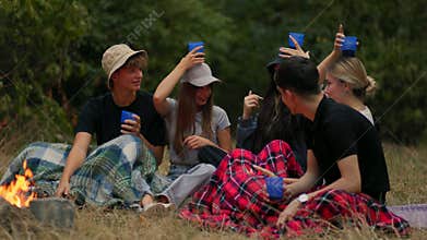 Group of cheerful young people hanging out by fire outdoors