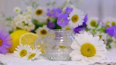 Empty glass jar surrounded by chamomile flowers and wildflowers on bright background with copy space