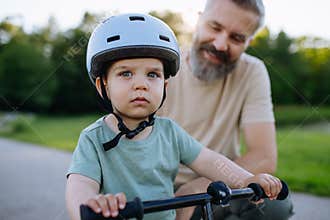 Father teaching toddler son to ride balance bike while wearing safety helmet.