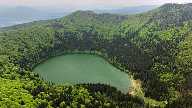 High-altitude aerial view of a round crater lake encircled by forest,