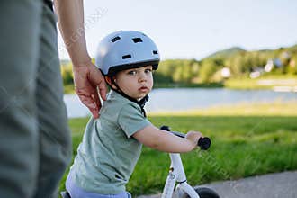 Father teaching toddler son to ride balance bike while wearing safety helmet.