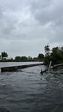 Stormy waters beside damaged riverside barrier beside overcast sky, with rough
