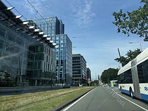 Modern glass office towers line wide urban street beside tram lane, with