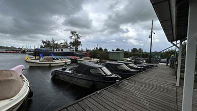 Rainy marina with moored boats beside wooden pier and covered deck under