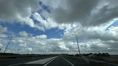 Wide motorway curve beneath dramatic cloud filled sky with streetlights