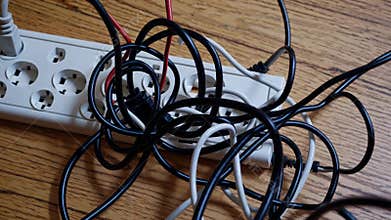 Cluttered cord situation. Disorganized cables on workspace surface. Messy electrical cords cluttered on desk. Chaotic