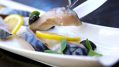 Lightly salted mackerel olives lemon microgreens white plate seafood closeup cutting fork knife