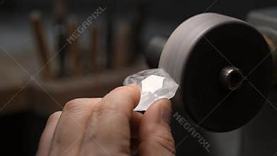 A Close up View of a Skilled Craftsman Hand Holding a Shiny Clear Diamond Crystal against a Spinning Polishing Wheel in a