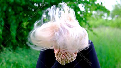 Middle aged blonde woman rubbing her nose with finger while reacting to irritation or seasonal allergy in garden