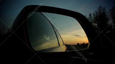 Driving with vivid sunset in rear mirror