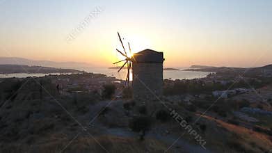Aerial drone circles historic stone windmill above Foca at sunset on Aegean coast in Turkiye, historic mill, stone tower, izmir