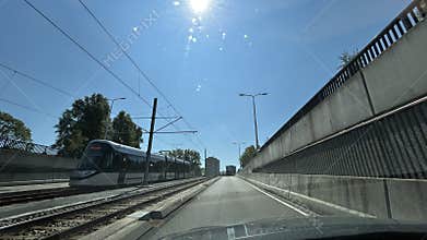 Sunlit urban tram corridor beside road and concrete retaining walls with overhead