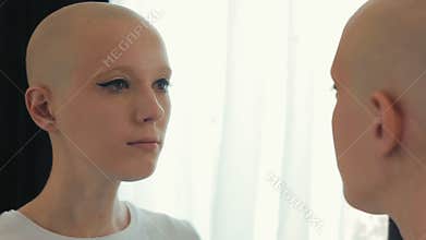 Sad woman suffering from cancer looking at herself in the mirror