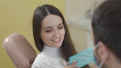 Young beautiful woman in the dental chair. After the procedure she looks in the mirror. The concept of a healthy smile.