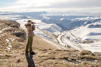 Beautiful blonde girl with a camera to take pictures of Caucasian mountains